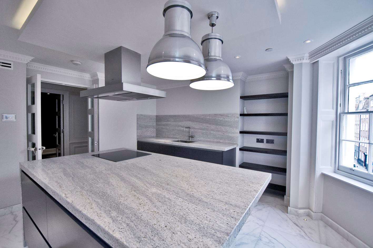 The completed kitchen at Soho Square with a stone island beneath industrial pendants.