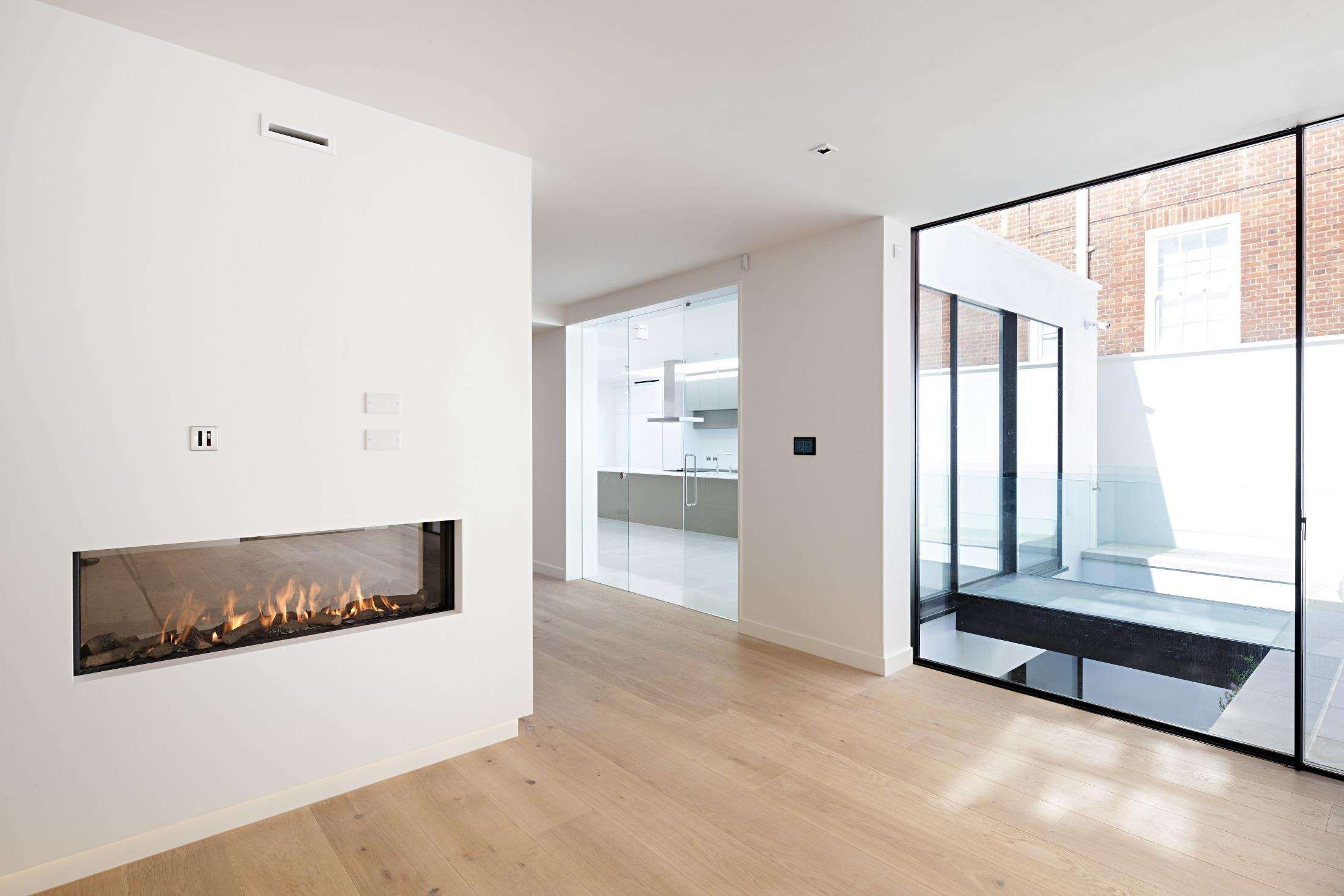 The living room at St John’s Wood with a linear fireplace and garden glazing.