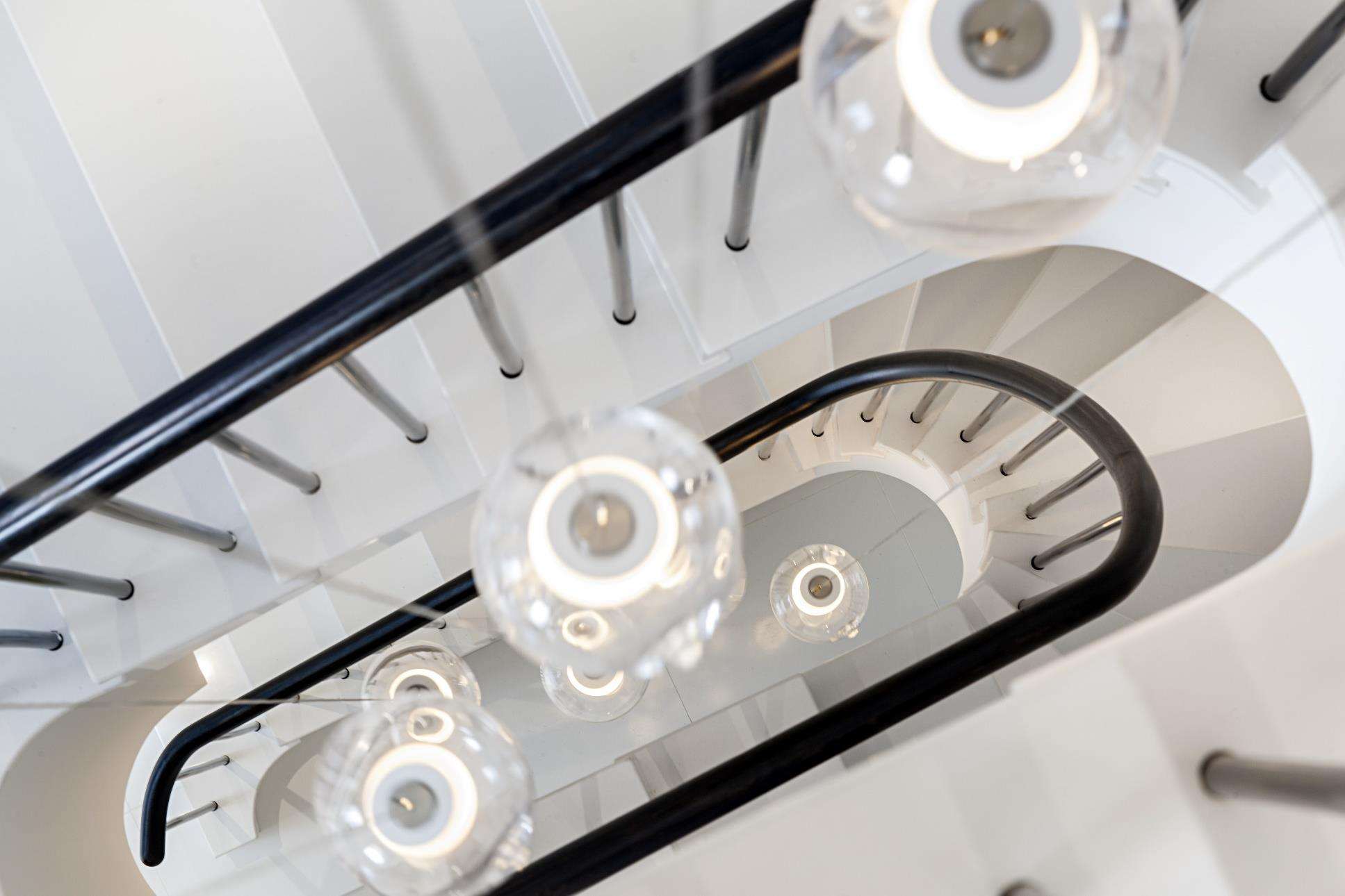The principal staircase at St John’s Wood photographed from above, spiralling around pendant lights.